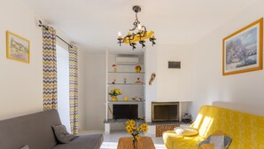 Una sala de estar con un sofá, un sofá amarillo, un televisor, una chimenea y una araña.