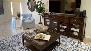 A living room with a TV, a blue armchair, a coffee table with books, a decorative plant, and a fish tank.