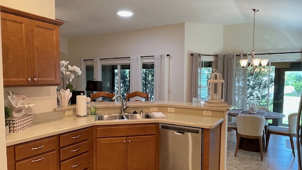 A kitchen with wooden cabinets, a dishwasher, and a dining area with a table and chairs.