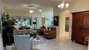 A spacious living room with a beige sofa, two armchairs, a coffee table, and a chandelier.