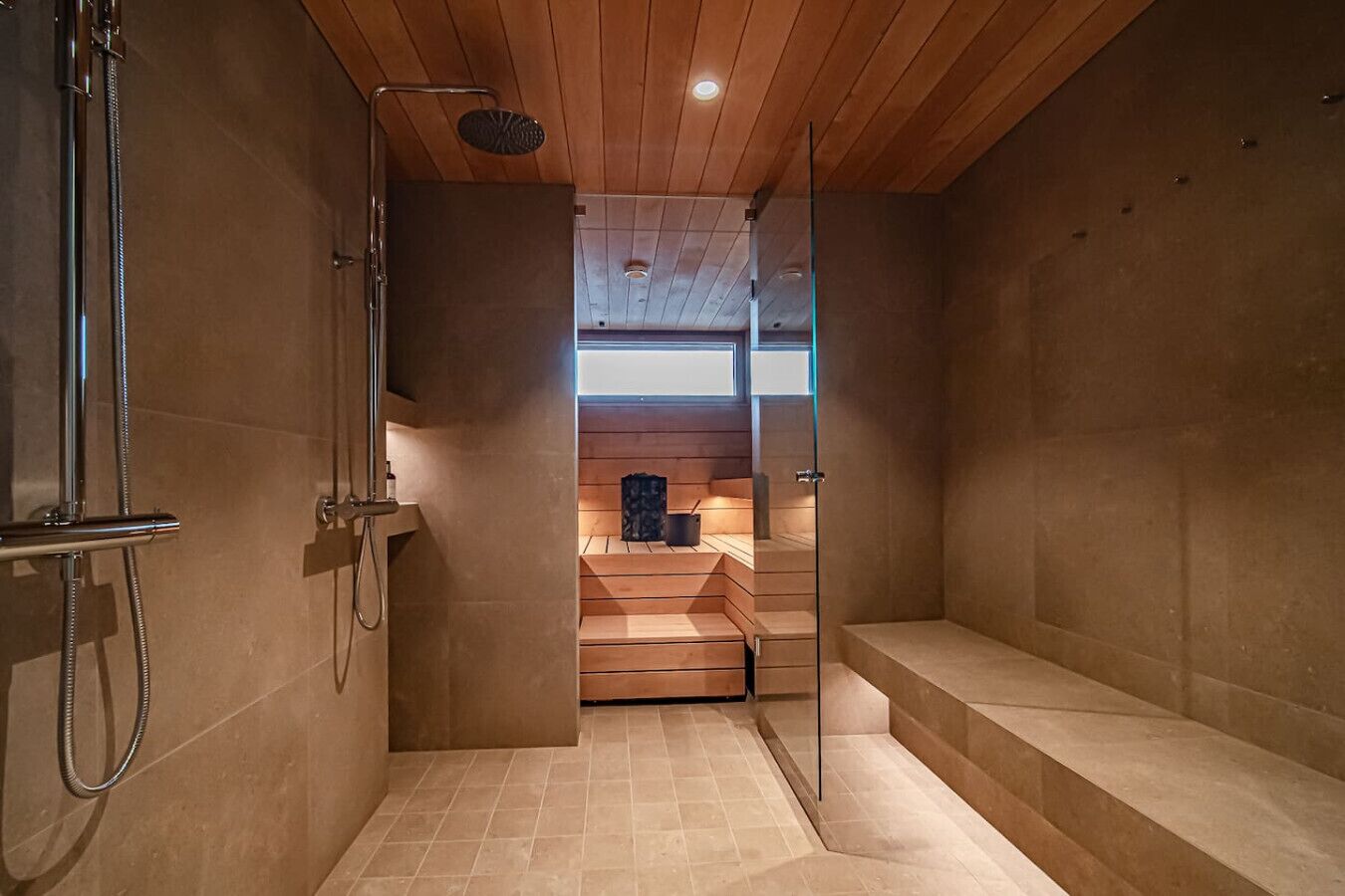 Un espace douche moderne avec une porte en verre, des marches en bois et, au fond, une salle de sauna visible.