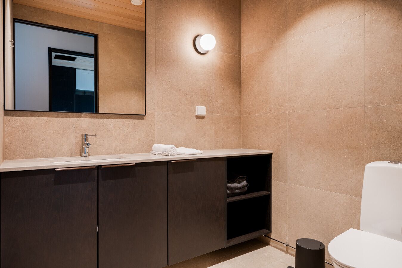 Een moderne badkamer met een grote spiegel, een wastafel, een toilet en een plank met handdoeken.