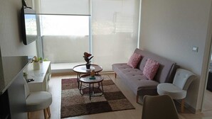 Un salon moderne comprenant un canapé, deux fauteuils, une petite table ronde agrémentée d’un objet décoratif, une table basse et un téléviseur fixé au mur.