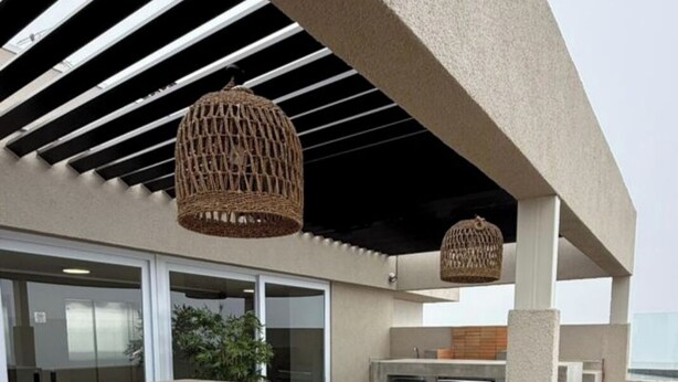 Un espace extérieur aménagé en terrasse, avec un bar en béton et des sièges, le tout abrité par une pergola agrémentée de luminaires en fibres tressées.