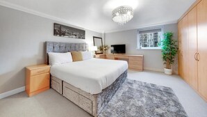 Ein Schlafzimmer mit einem Bett, Nachttischen, einem Fernseher, einem Fenster, einer Chandelier und einer Zimmerpflanze.