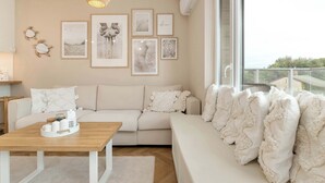 Ein modernes Wohnzimmer mit einem beigen Sofa, einem Holztisch und einem großen Fenster mit Blick auf Grünflächen.