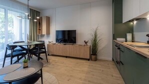 Une cuisine moderne dotée d’un four encastré, un coin repas avec une table ronde et des chaises, et une grande fenêtre agrémentée de rideaux légers.