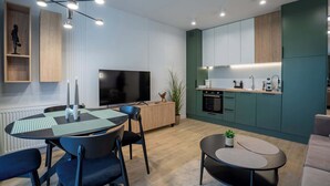 Une cuisine moderne dotée d’un four et d’un micro-ondes encastrés, un coin repas avec une table ronde et des chaises, et un téléviseur fixé au mur.