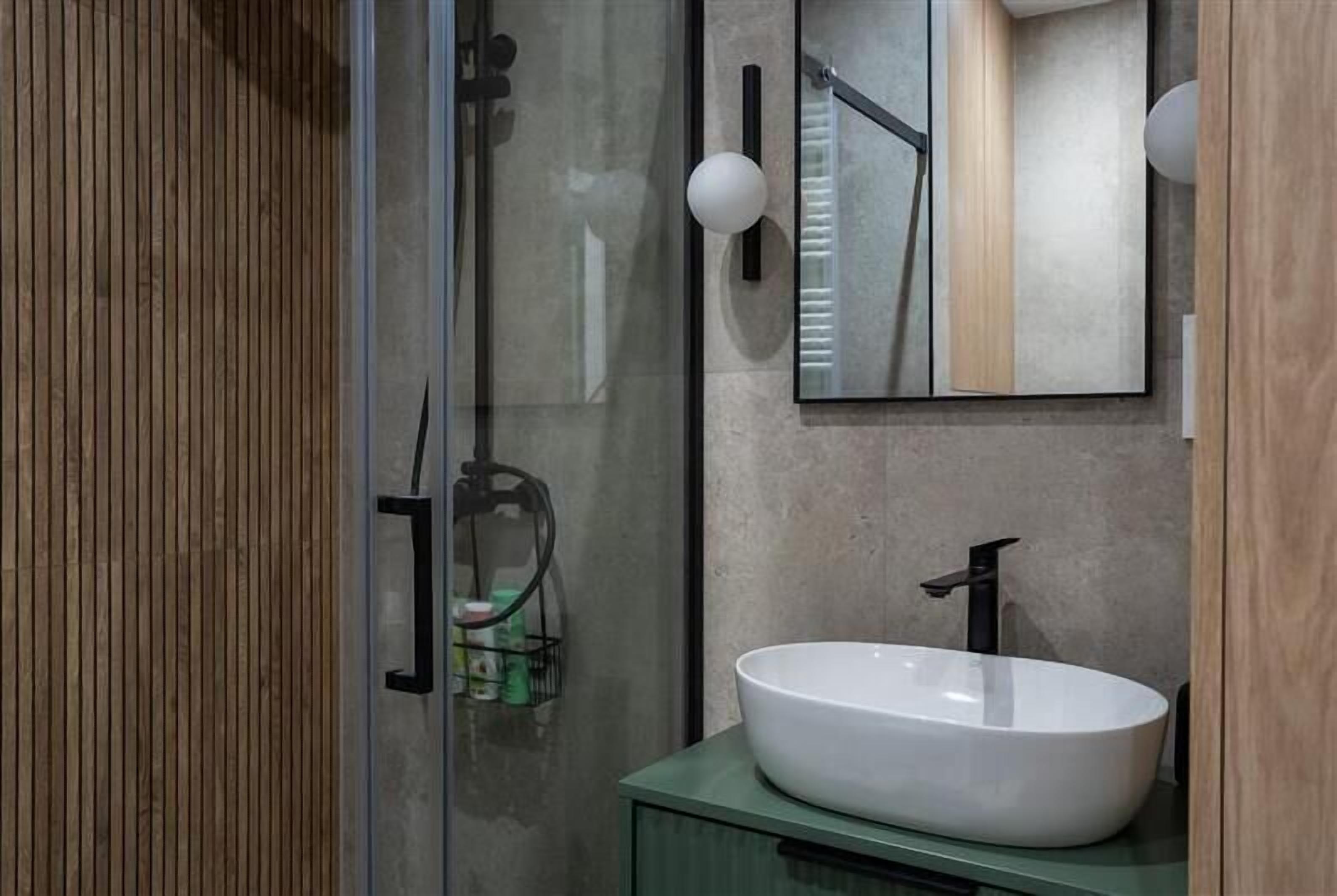 Un baño moderno con cabina de ducha de vidrio, un lavamanos blanco y un mueble de tocador de madera.