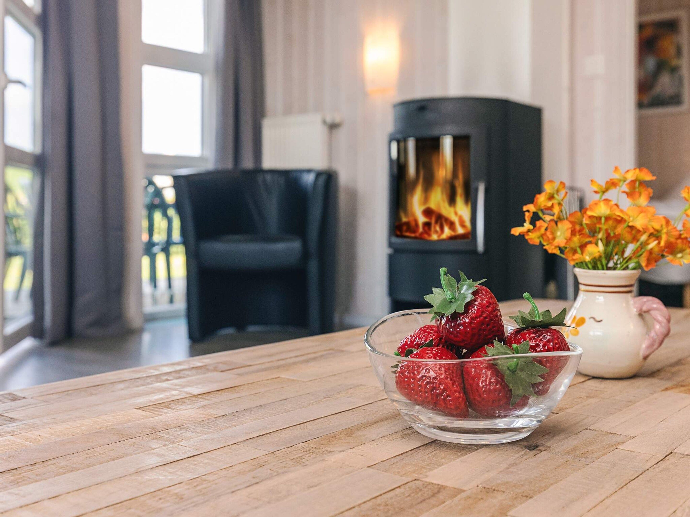 A room with a fireplace, a black chair, and a bowl of strawberries on a wooden table.