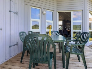 A covered outdoor area with a table and chairs, a bottle of water, and a view of the interior through open doors. - 4 Star Holiday Home in Friedrichskoog (Friedrichskoog)