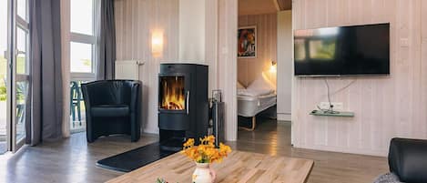A modern living room with a fireplace, a flat-screen TV, a dining table with flowers, and a comfortable seating area.