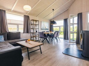 A spacious living area with a sofa, coffee table, dining table, and chairs. There is a bookshelf, a painting, and a fireplace.
