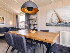 A dining area with a wooden table, black chairs, a black pendant light, and a sailboat painting on the wall. - 4 Star Holiday Home in Friedrichskoog (Friedrichskoog)