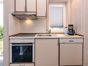 A compact kitchen with a built-in oven, a dishwasher, a coffee maker, and a window with blinds.