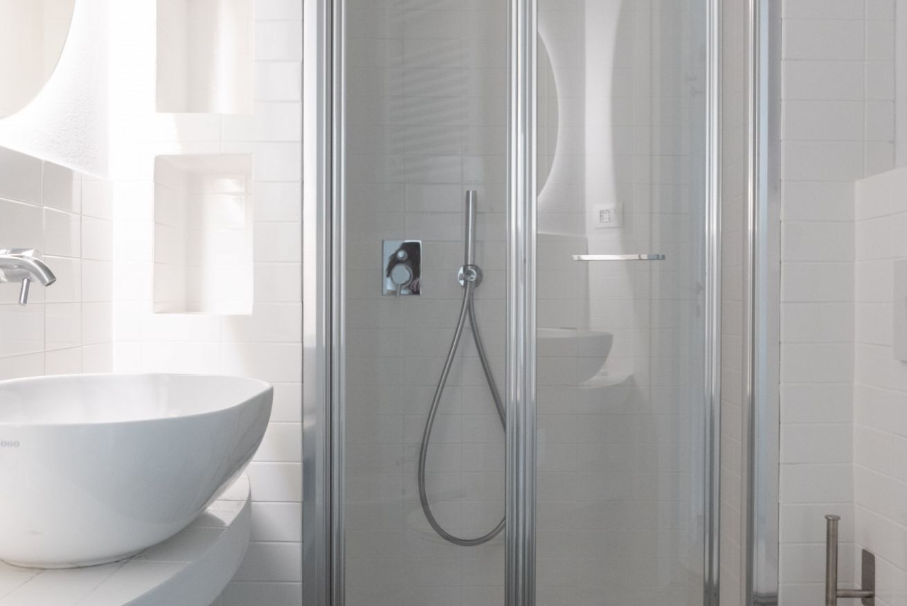 A modern bathroom with a glass-enclosed shower, a white sink, and a tiled wall.