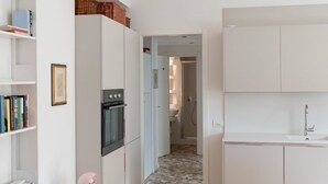 Una cuina moderna amb armaris blancs, un forn negre i un salvassecs revestit de rajoles.