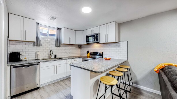 A compact kitchen with white cabinets, a microwave, a stove, and a sink. There are three wooden stools at the island. - Large family home near Hidden Lake (Denver)