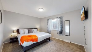 A bedroom with a bed, nightstands, a window with curtains, a wall-mounted TV, and a ceiling light. - Spacious Family Home in Denver with large yard (Denver)