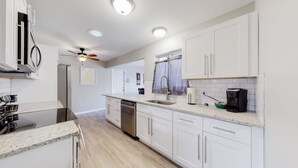 A modern kitchen with white cabinets, a stainless steel refrigerator, a dishwasher, and a coffee maker. - Spacious Family Home in Denver with large yard (Denver)