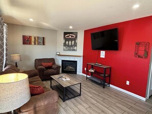 A living room with a red wall, a fireplace, a sofa, a coffee table, and a TV mounted on the wall. - Spacious Family Home in Denver with large yard (Denver)