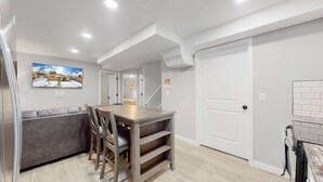 A modern kitchen with a wooden table and chairs, a grey sofa, and a staircase leading to another room. - Affordable four bedroom Family Denver home (Denver)