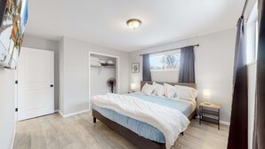 A bedroom with a bed, bedside tables, a window with curtains, a ceiling light, and a door. - Affordable four bedroom Family Denver home (Denver)