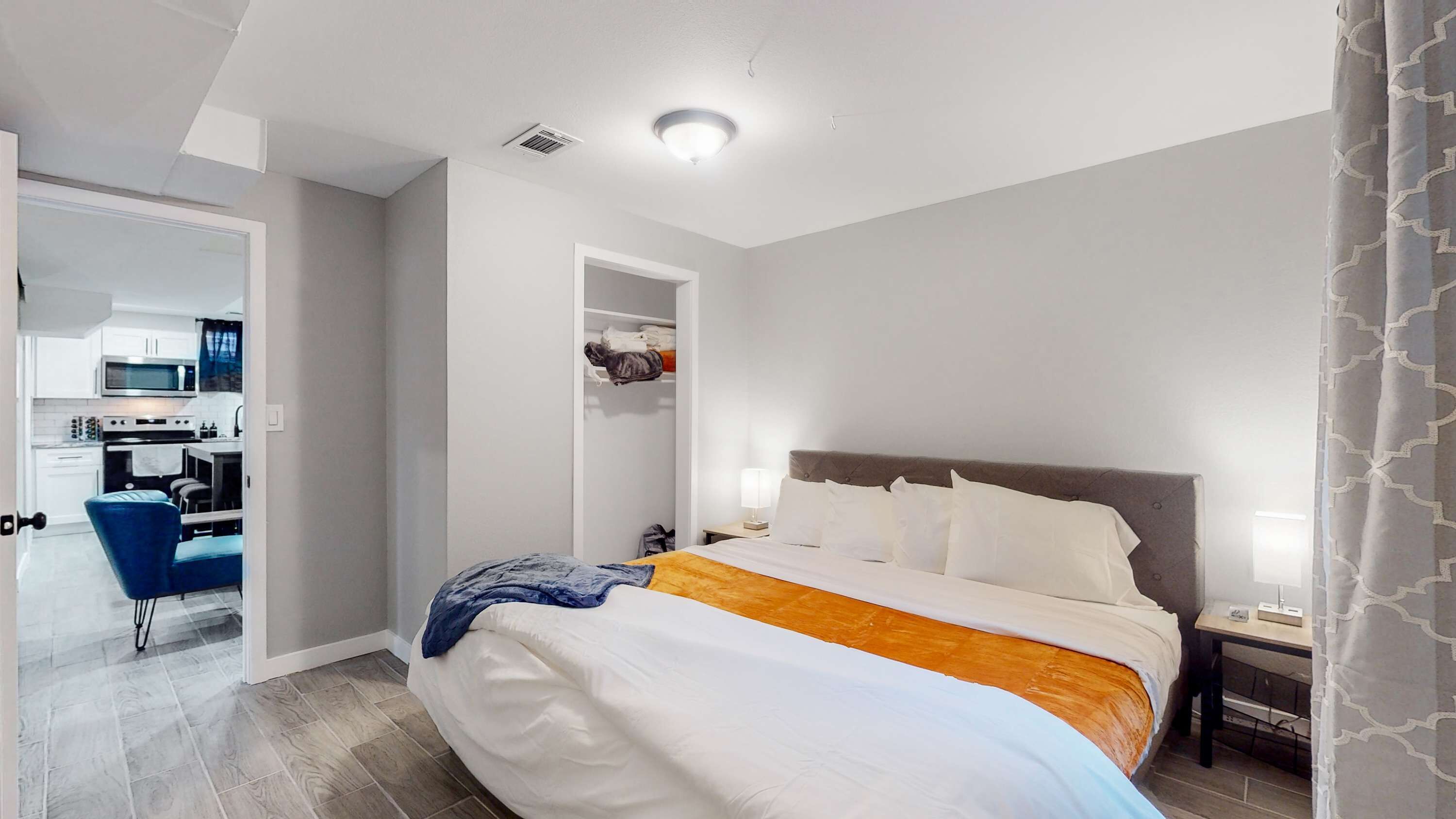 A hotel room with a bed, bedside table, and a view of the kitchen.