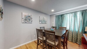 A dining area with a wooden table and chairs, two floral paintings on the wall, and a window with patterned curtains. - Unique Family Home in Denver (Denver)