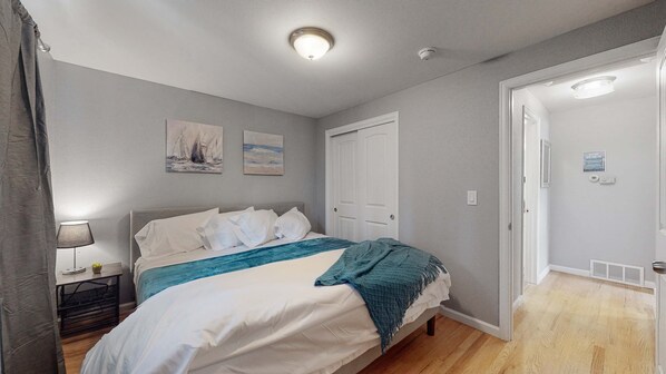Un dormitorio con cama, mesita de noche, lámpara y puerta.
