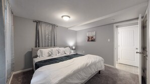A bedroom with a bed, a nightstand, a lamp, a painting, and a door.