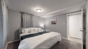 A bedroom with a bed, a nightstand, a lamp, a painting, and a door. - Unique Family Home in Denver (Denver)