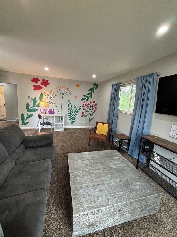 A living room with a grey sofa, a wooden coffee table, a TV, and a wall with floral decorations.