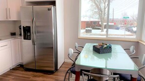 A modern kitchen with white cabinets, a stainless steel refrigerator, and a glass-top dining table with chairs.