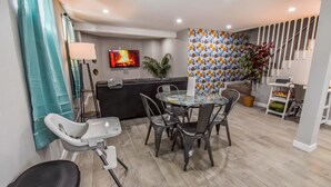 A modern hotel room with a dining area, a TV, a sofa, and a patterned wall.