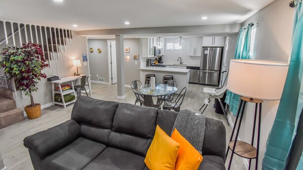 A modern living room with a black leather sofa, a dining table, and a kitchen area with white cabinets and stainless steel appliances.