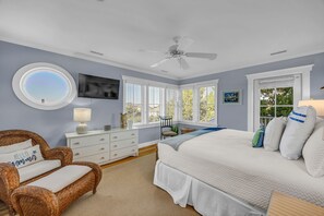 A bedroom with a large bed, a wicker chair, a dresser, and a ceiling fan.