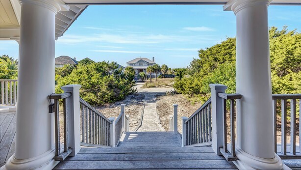 A view from a covered porch with white columns and a wooden staircase leading to a house. - Escape to Beacon Point Inn on Bald Head Island, NC-5 Bedrooms. Oceanview (Bald Head Island)