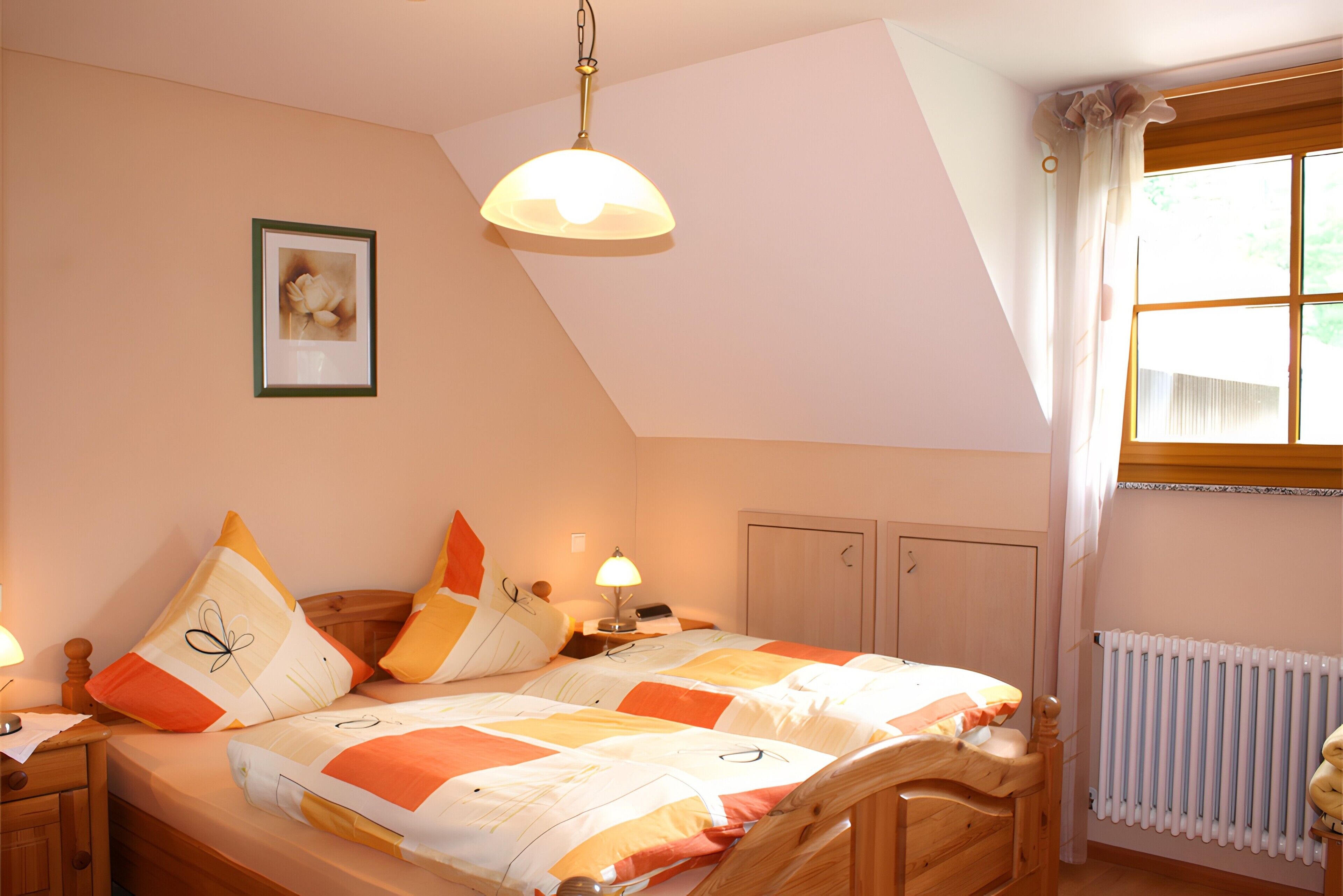 Ein Schlafzimmer mit Bett, Nachttischen, einer Lampe, einem Bild an der Wand und einem Fenster mit Vorhängen.