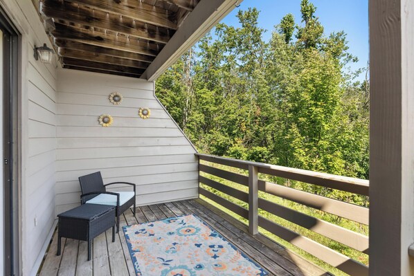 A wooden deck with a railing, a small table with a chair, and a decorative rug.