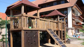 A wooden play structure with a slide and climbing wall, adjacent to a building with a red-tiled roof. - Holiday Apartment 'Landsitz, 55 sqm' with Shared Terrace, Shared Garden and Wi-Fi (Elzach)