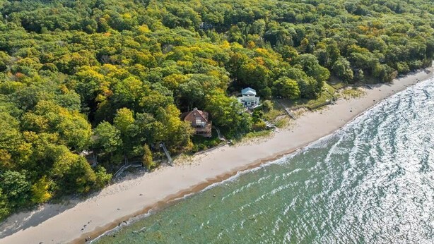 Ett flygbildsbild av en fastighet vid kusten med en tät skog, en sandstrand och ett hus nära vattnet.