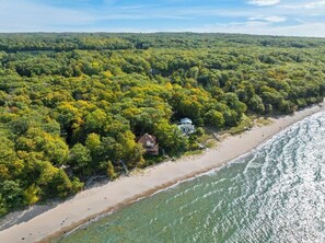 An aerial view of a coastal property with dense forest, a sandy beach, and a house near the water.