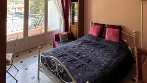 Een slaapkamer met een bed, een stoel, een nachtkastje, een raam met gordijnen en uitzicht op het omliggende landschap.