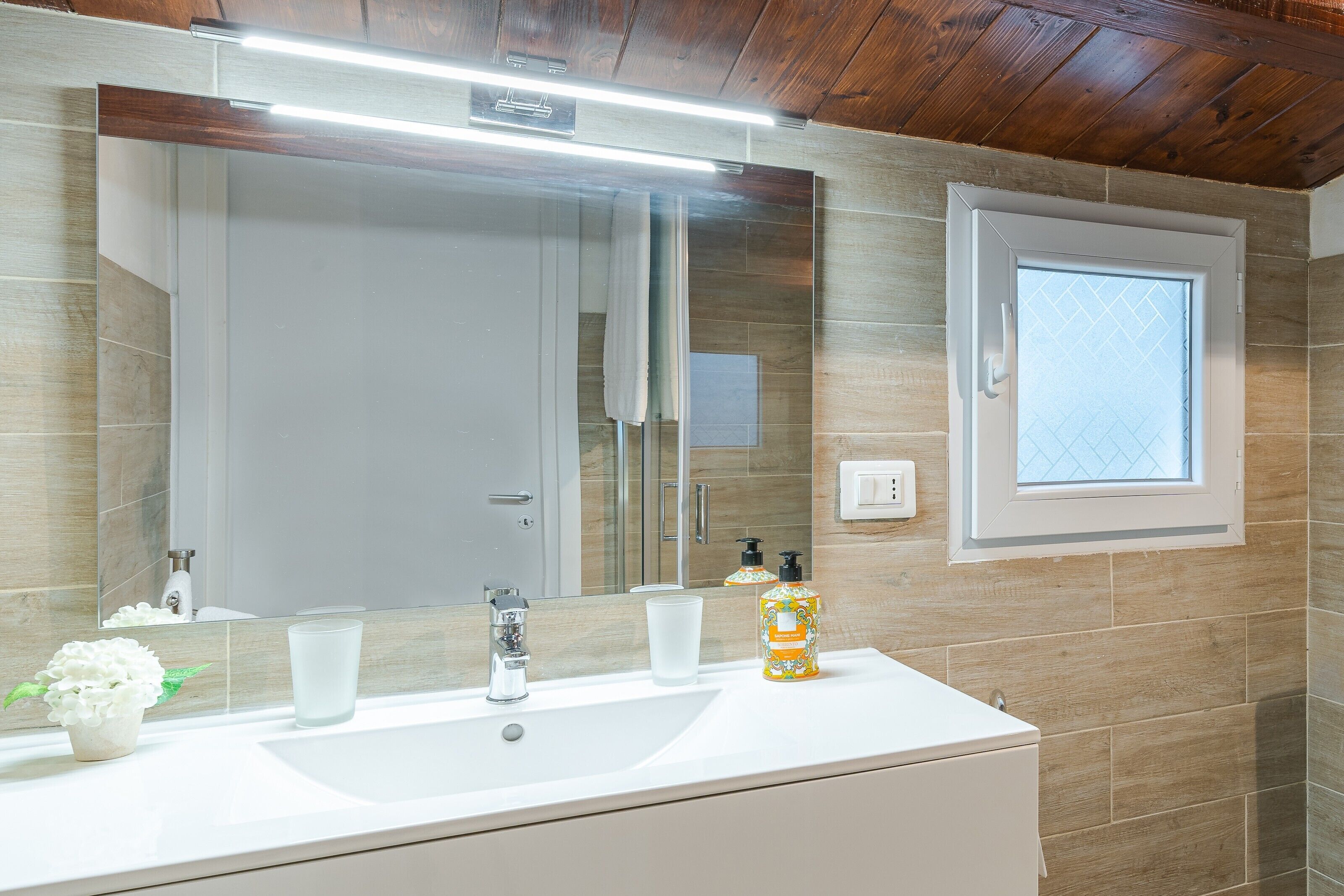 A bathroom with a white sink, a mirror, a window, and a potted plant.