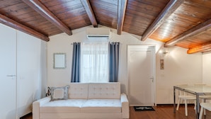 Um quarto com sofá branco, vigas de madeira no teto, mesa de jantar com cadeiras e uma porta.