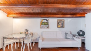 Sala de estar com mesa de jantar de vidro, sofá branco, vigas de madeira no teto e duas obras de arte emolduradas na parede.