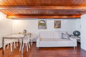Un salon avec une table à manger en verre, un canapé blanc, des poutres en bois au plafond et deux œuvres d’art encadrées accrochées au mur.