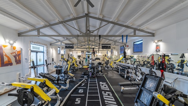 Uma academia com diversos equipamentos de exercício, um ventilador de teto e uma placa na parede.