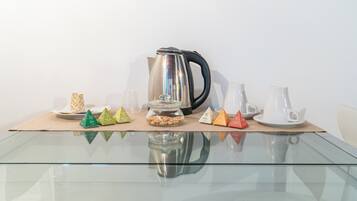 Ein Glastisch mit einem Edelstahlkocher, weißen Tassen und kleinen, pyramidenförmigen Behältern.